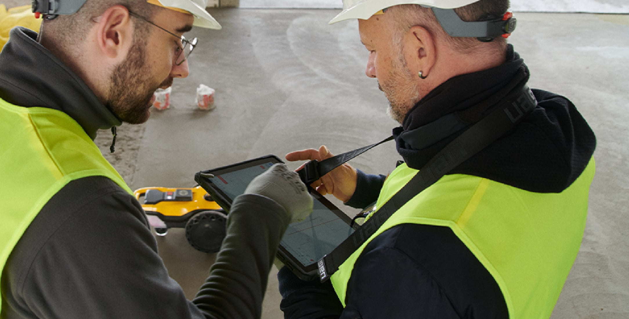 Two construction workers on a construction site talking over a tablet.