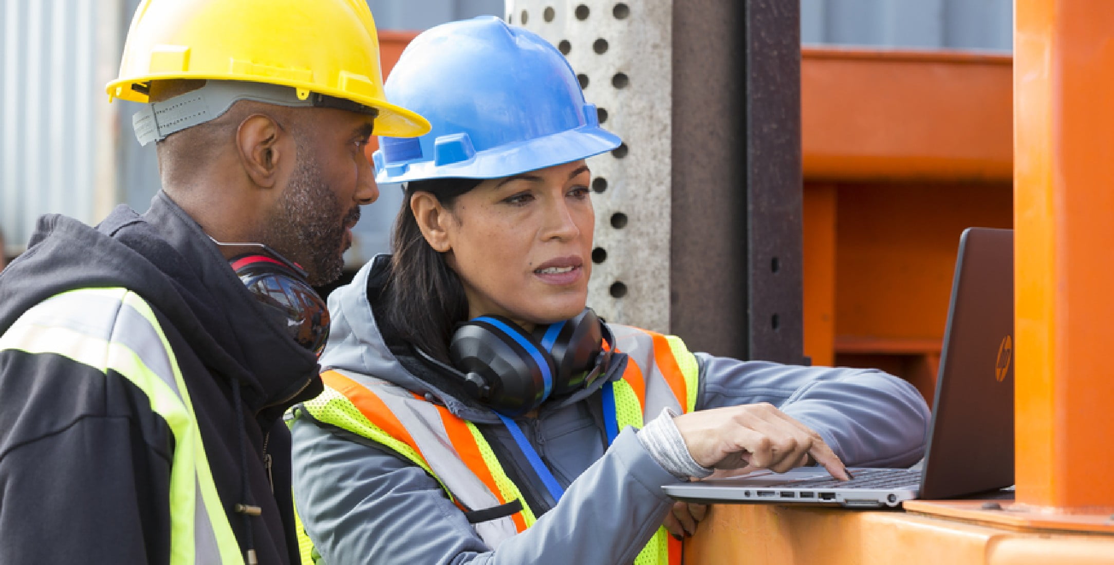 Two construction workers using a HP laptop on a construction site.