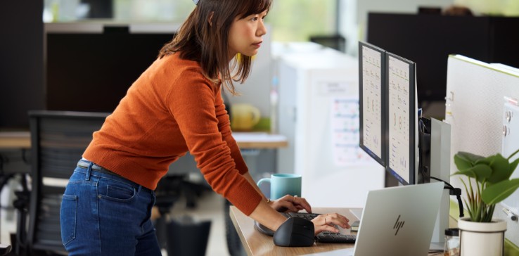 Woman at office desk looking at two HP monitors.